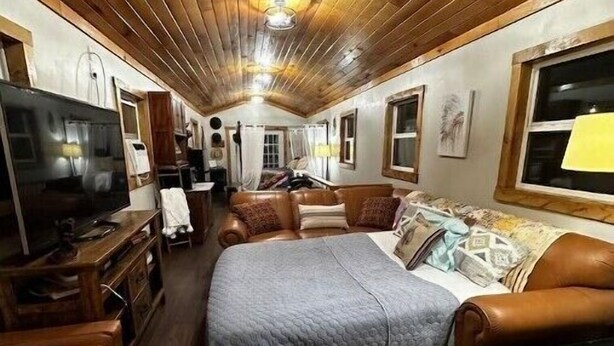 Una cabaña acogedora y bien iluminada con techo de madera, una cama grande, un televisor y una chimenea.