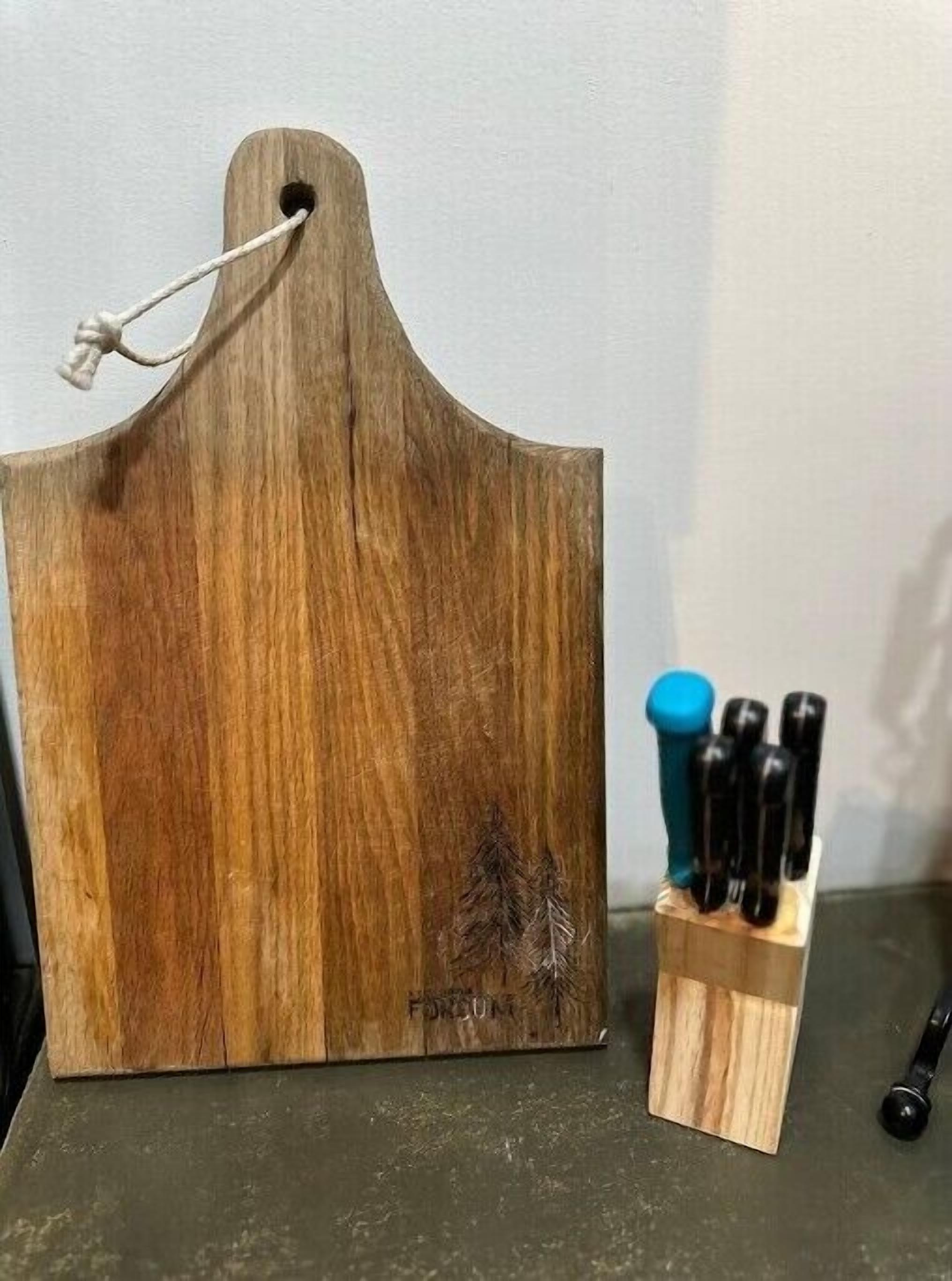 A wooden cutting board with a handle and a knife block with several knives.