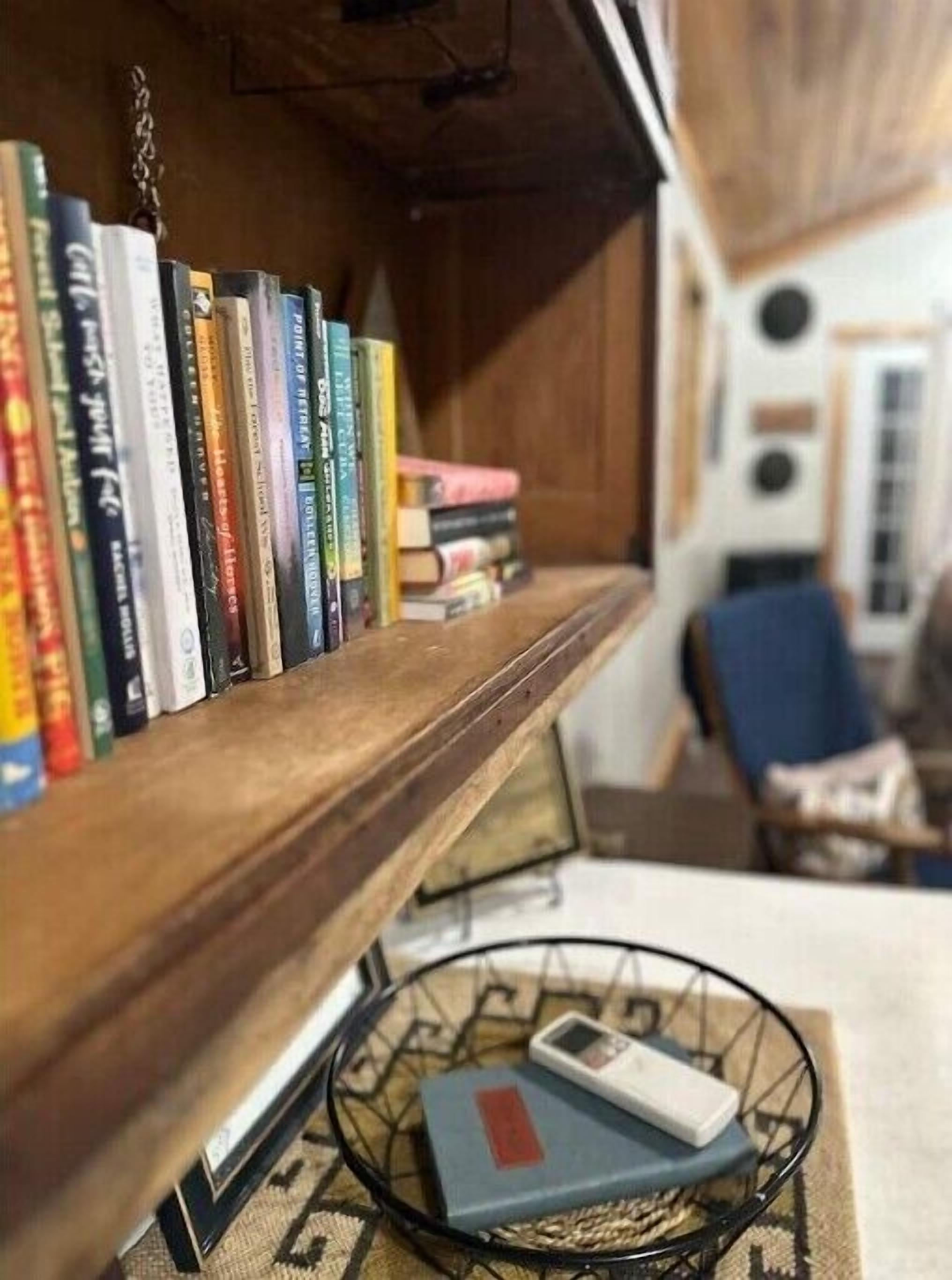 A bookshelf filled with books, a small table with a book and a remote, and a chair in the background.
