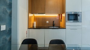 A modern kitchen with wooden cabinets, a black countertop, a sink, a microwave, and a glass table with chairs.
