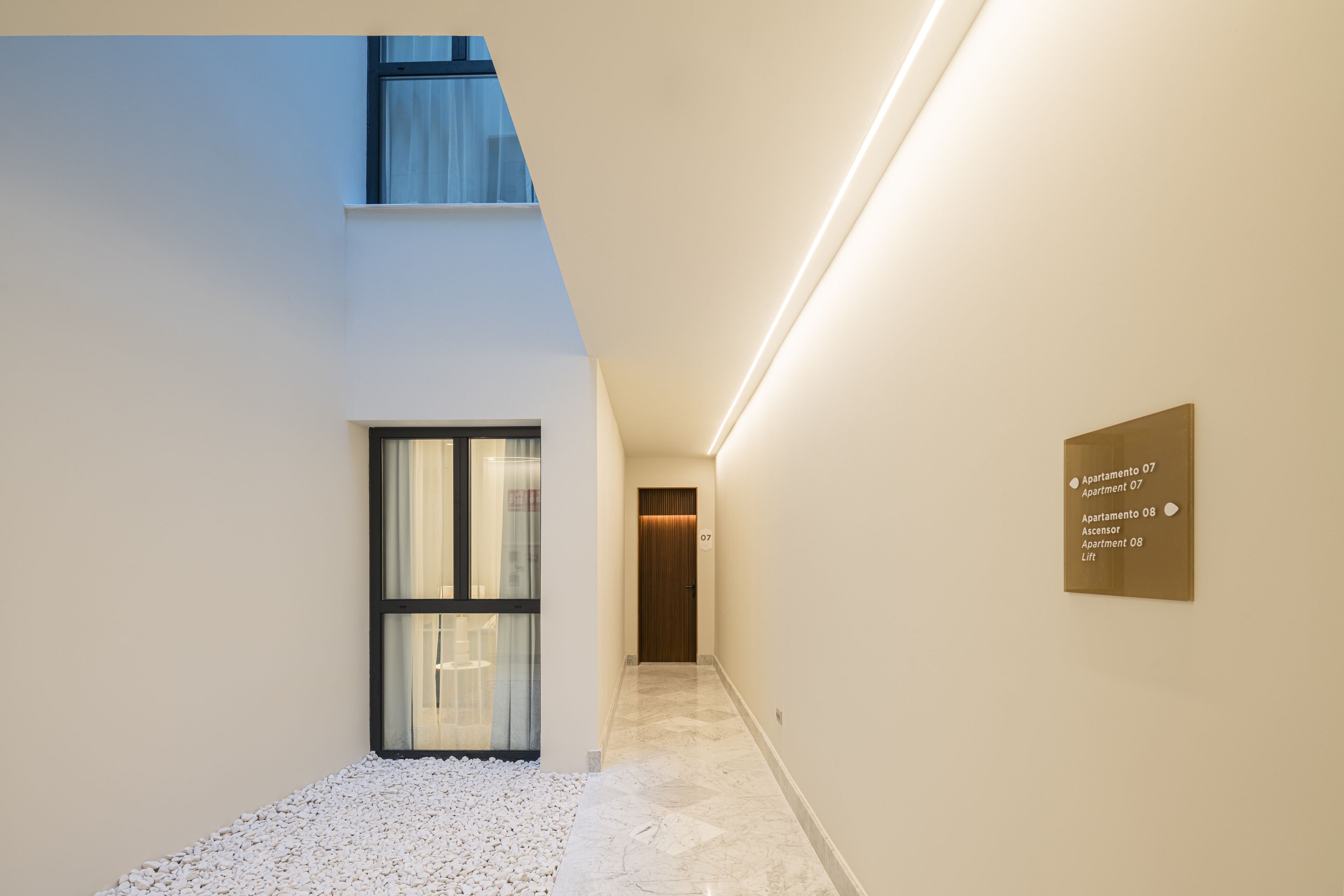 A modern hallway with a glass door, a sign indicating apartments 07 and 08, and a lift.