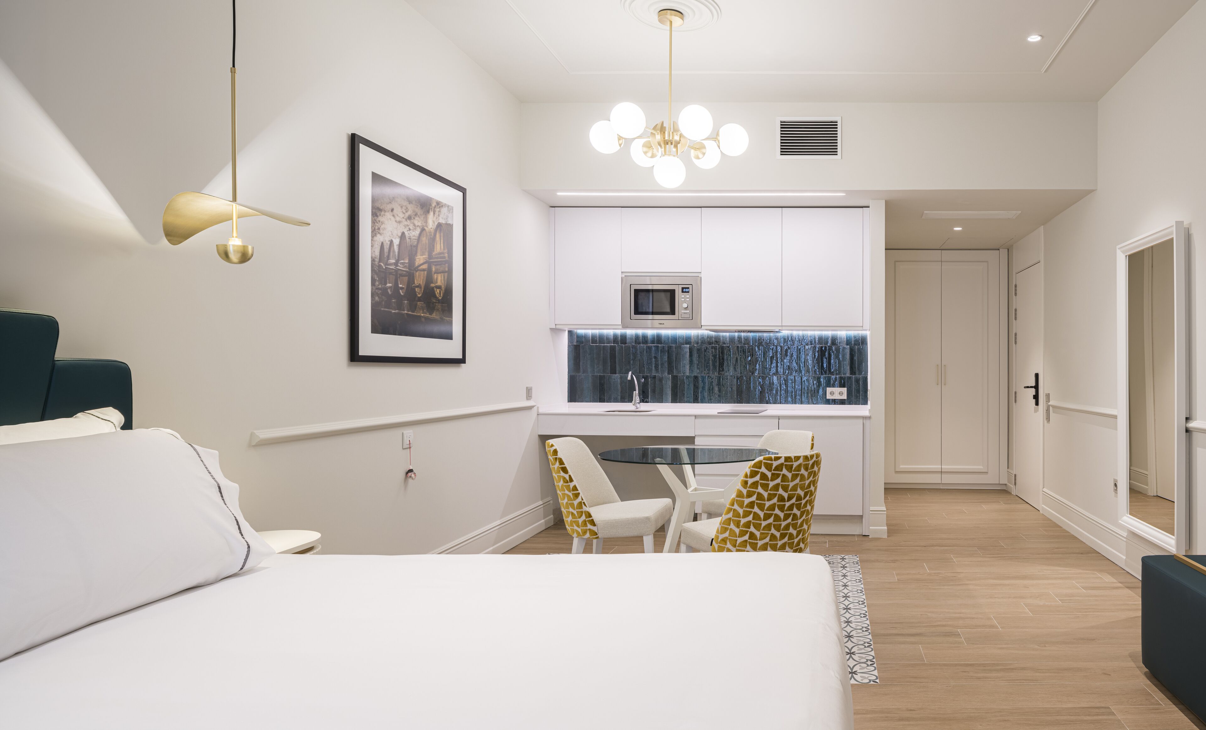 Un dormitorio moderno con una cama grande, un escritorio con sillas, una kitchenette y un baño.