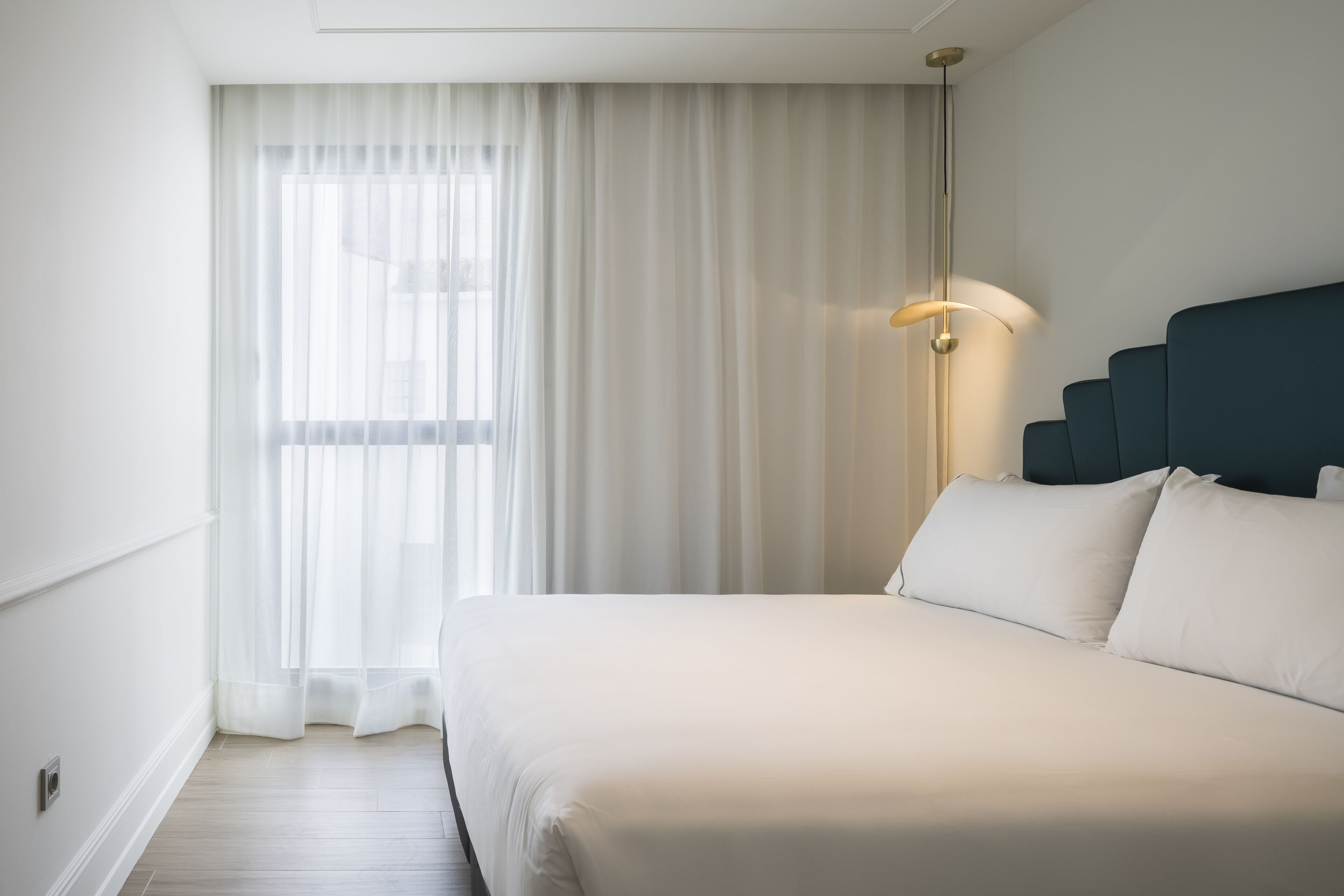A hotel room with a large bed, a bedside lamp, and sheer curtains.