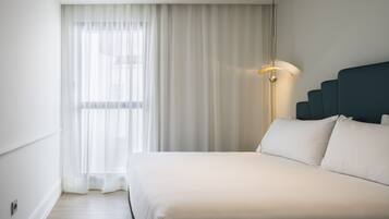 A hotel room with a large bed, a bedside lamp, and sheer curtains.