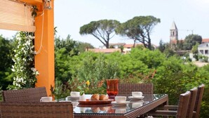 An outdoor dining area with wicker furniture, a glass table, and a view of a town with a church tower. - Charming Villa Diora with a swimming pool and wellness area (Karojba)