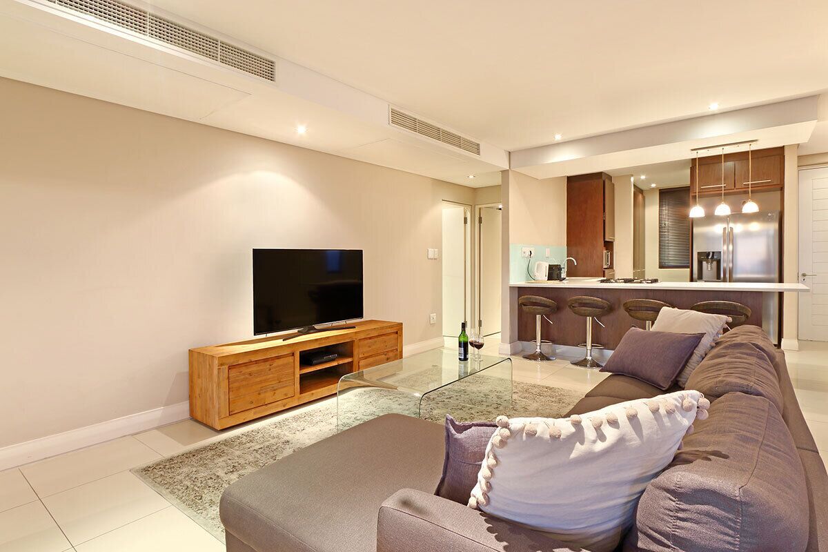 A modern living room with a flat-screen TV, a wooden entertainment unit, a brown sofa, and a glass coffee table.