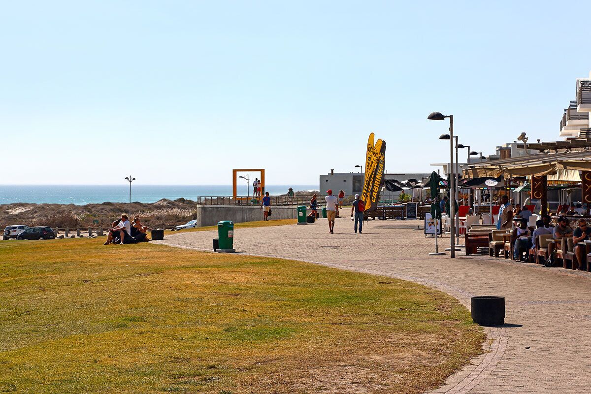 A coastal walkway with outdoor seating, a view of the sea, and a distinctive yellow structure.