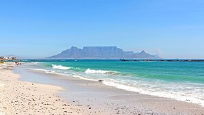 A beach with clear turquoise waters, a rocky shoreline, and a prominent mountain in the background.