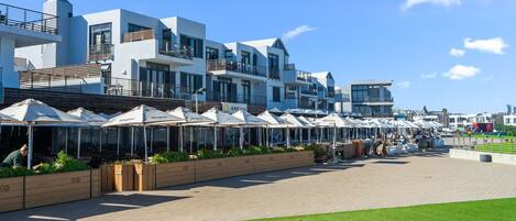 A modern hotel with multiple balconies, outdoor seating areas, and a paved walkway.