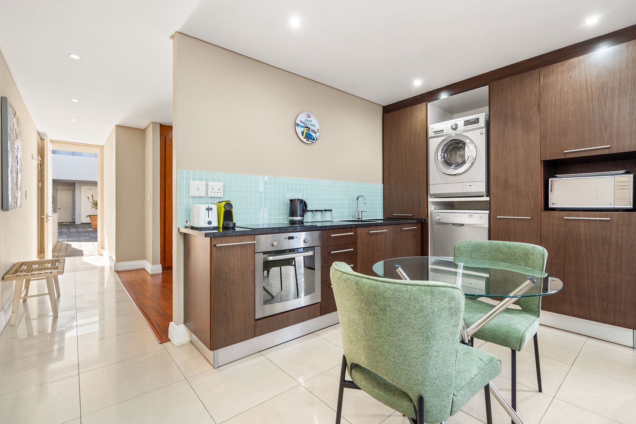 Una cocina moderna con comedor, que incluye cafetera, hervidor y un reloj en la pared.