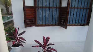 A balcony with two potted plants, a window with wooden shutters, and a tiled floor. - Nutmeg House Zanzibar (Jambiani)