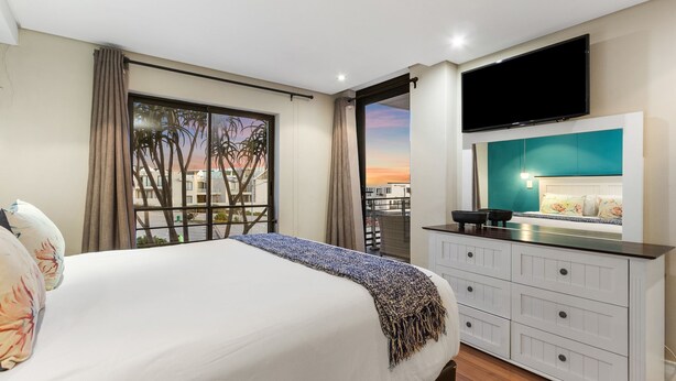 Une chambre d’hôtel avec un lit, une télévision, un balcon avec vue et une commode blanche.
