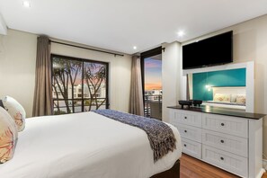 A hotel room with a bed, a TV, a balcony with a view, and a white dresser.