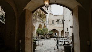 An outdoor courtyard with stone flooring, tables, chairs, and potted plants. - Schloss Freudenstein (Appiano Sulla Strada del Vino)