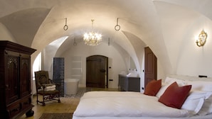 A bedroom with a large bed, a wooden wardrobe, a chair, and a chandelier. - Schloss Freudenstein (Appiano Sulla Strada del Vino)