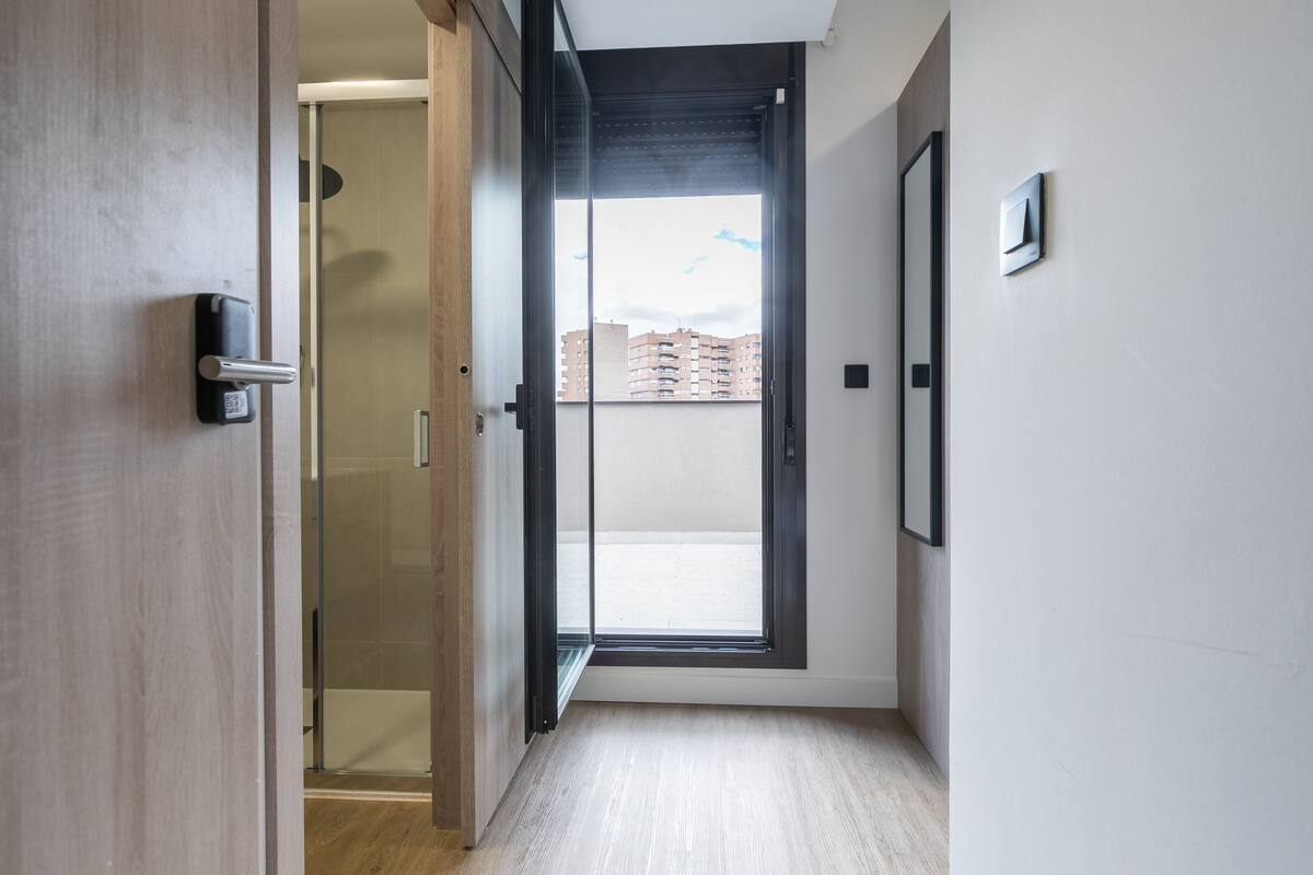 A modern interior with a wooden door, a glass door leading to a balcony, and a framed picture on the wall.