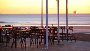 An outdoor dining area with tables and chairs, overlooking the sea with a ship in the distance.