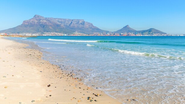 A beach with clear waters, a sandy shore, and distant mountains.