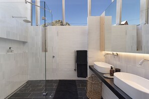 Ein modernes Badezimmer mit Duschkabine aus Glas, zwei Waschbecken und einem großen Spiegel.
