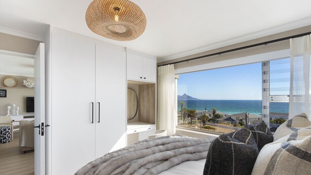 A bedroom with a large window offering a view of the sea and a mountain.