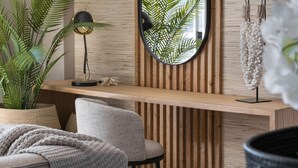A modern living room with a wooden wall, a round mirror, a black floor lamp, and a potted plant.