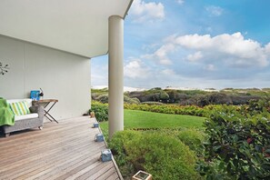A covered outdoor area with a wooden deck, a sofa, a small table, and a chair.