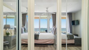 A bedroom with a large bed, a TV, and a view of the ocean.