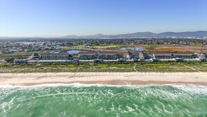 A coastal hotel with multiple buildings, a beachfront, and a view of the ocean and distant mountains.