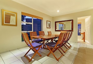 A dining area with a wooden table and chairs, large windows, and a mirror on the wall.