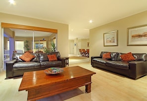 A living room with two leather sofas, a wooden coffee table, and a dining area in the background.
