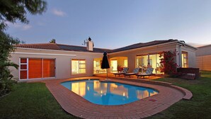 A residential property with a swimming pool, a covered patio, and a well-maintained lawn. - Durham Close 31 - Four Bedroom House, Sleeps 8 (Cape Town)