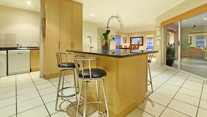 A modern kitchen with a central island, bar stools, and a dining area visible through a glass door. - Durham Close 31 - Four Bedroom House, Sleeps 8 (Cape Town)