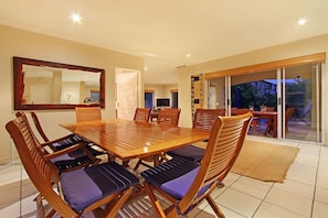 A dining area with a large wooden table, six chairs with cushioned seats, a mirror on the wall, and a view through a glass door to an outdoor patio.