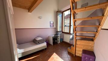 Habitación pequeña con cama, escritorio, silla, ventana y una escalera de madera.