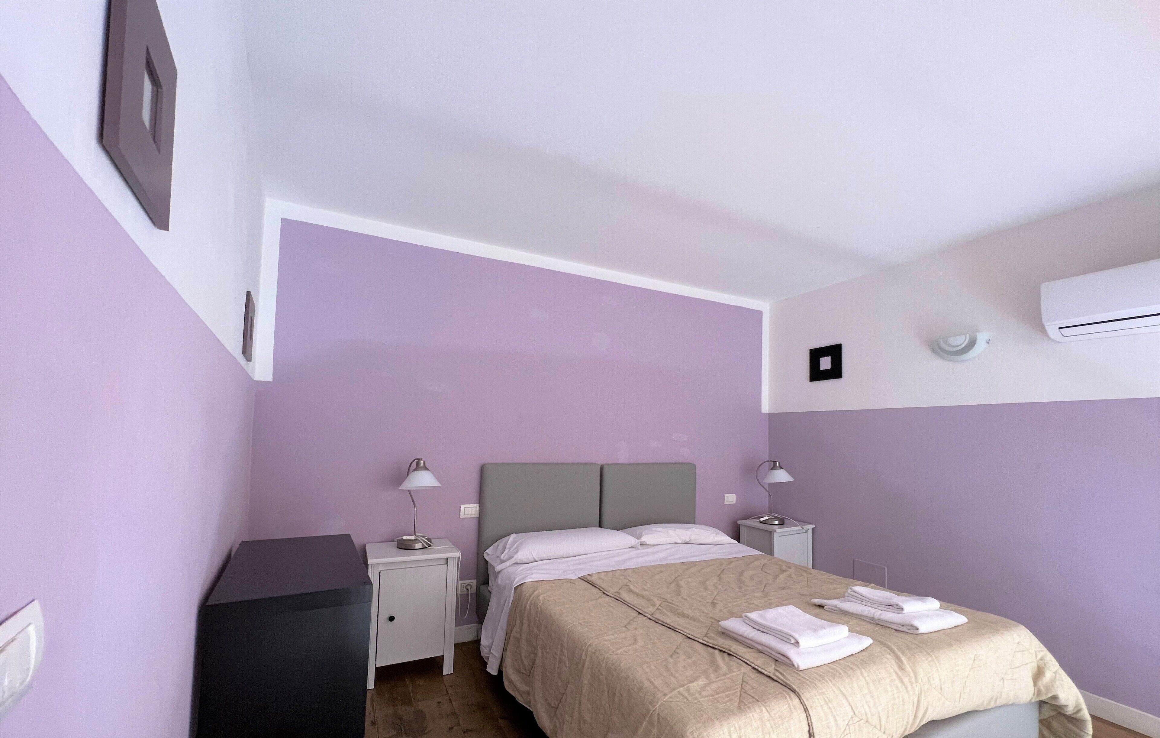 Un dormitorio con cama, mesitas de noche, lámpara, equipo de aire acondicionado e interruptor de luz en la pared.