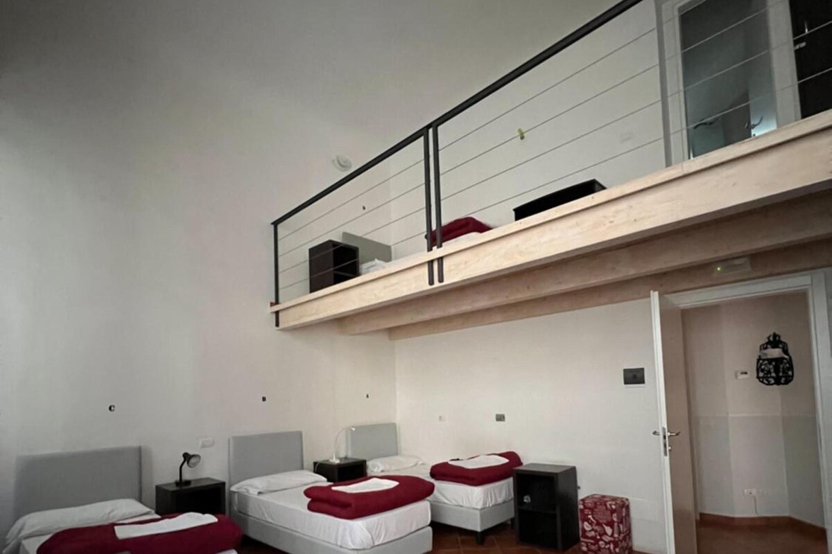 A room with two beds, a desk, a chair, a small table, and a door leading to another room.