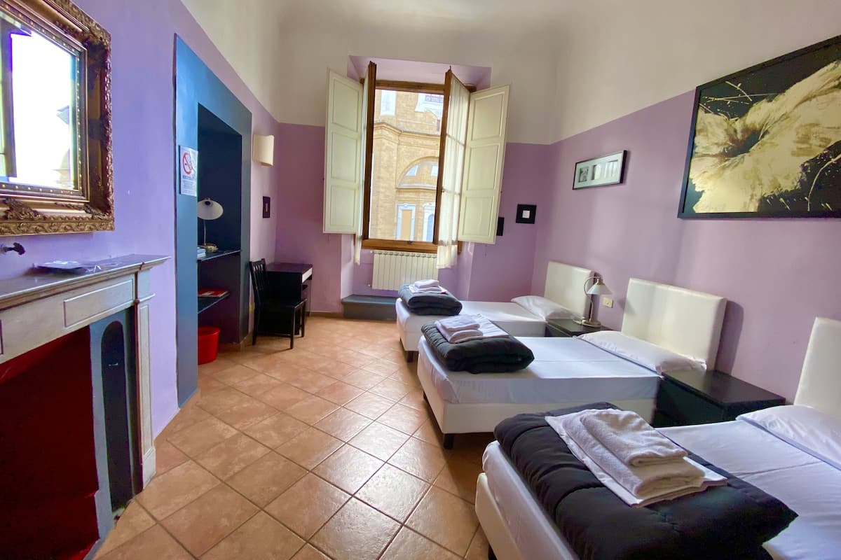 Una habitación con dos camas, un escritorio, una silla, una ventana con cortinas y un cuadro en la pared.