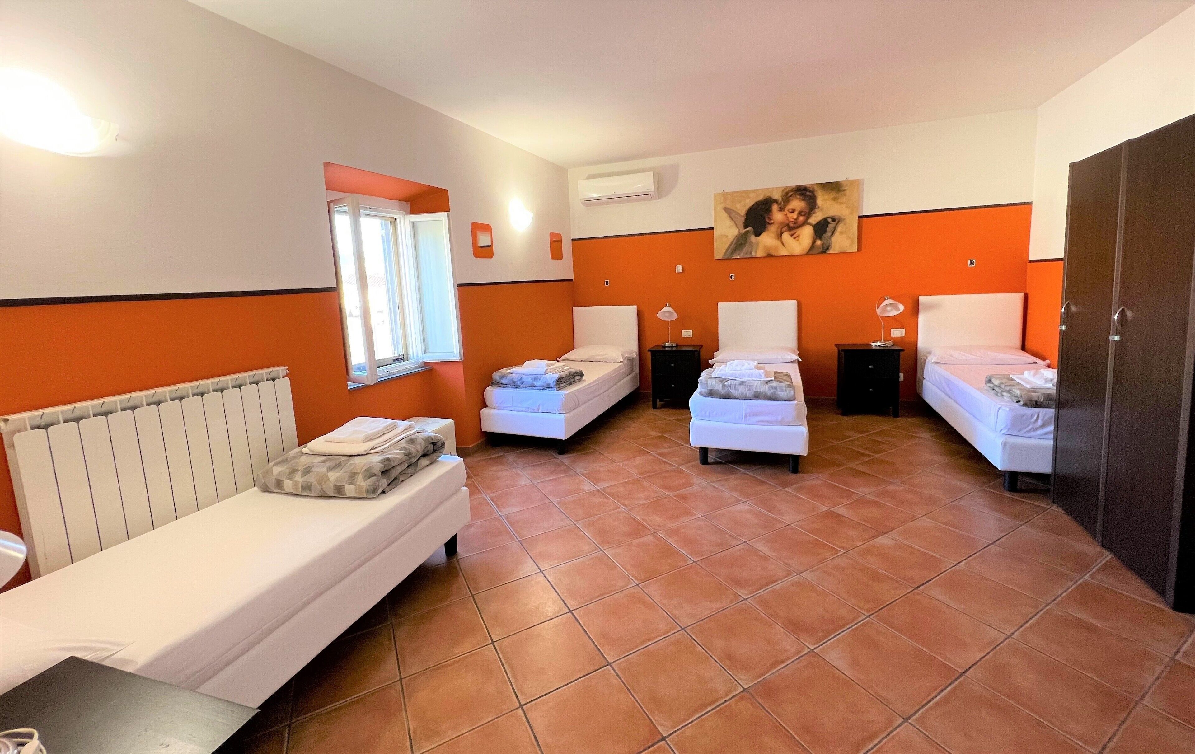 Habitación de hotel con tres camas individuales, un radiador, un equipo de aire acondicionado, una ventana y un cuadro en la pared.