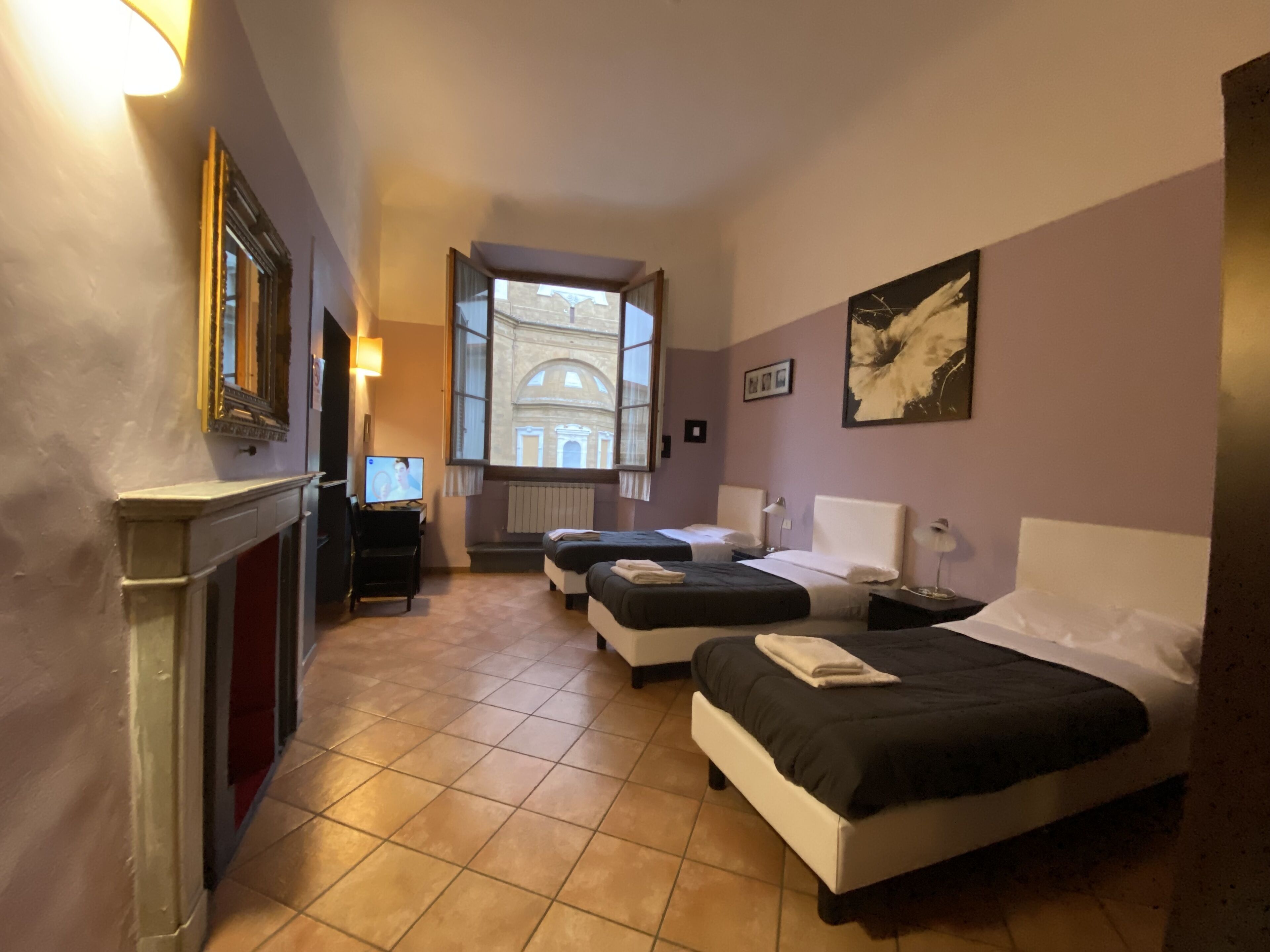 Habitación de hotel con dos camas, televisión, chimenea y vista a un edificio por la ventana.