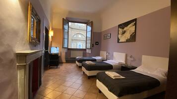 Habitación de hotel con dos camas, televisión, chimenea y vista a un edificio por la ventana.