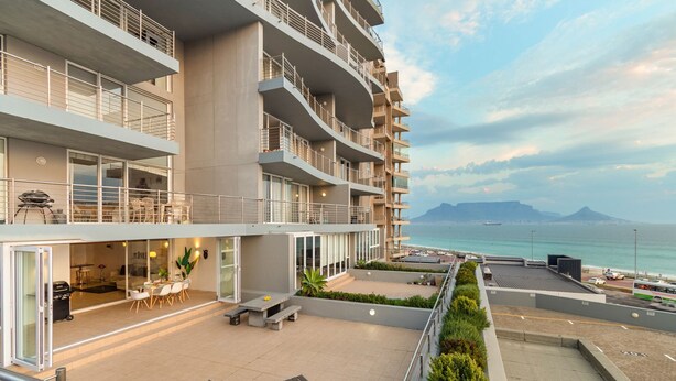 Un hotel moderno de varios pisos con balcones, mobiliario exterior y vista al mar.