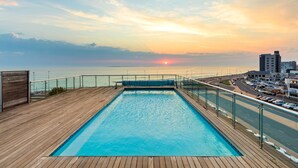 Una piscina con cubierta de madera y vistas a la puesta de sol sobre el océano.