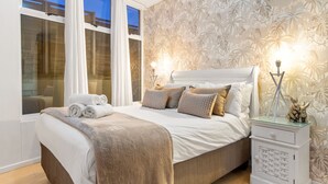 Un dormitorio con cama, mesita de noche y ventana con cortinas.