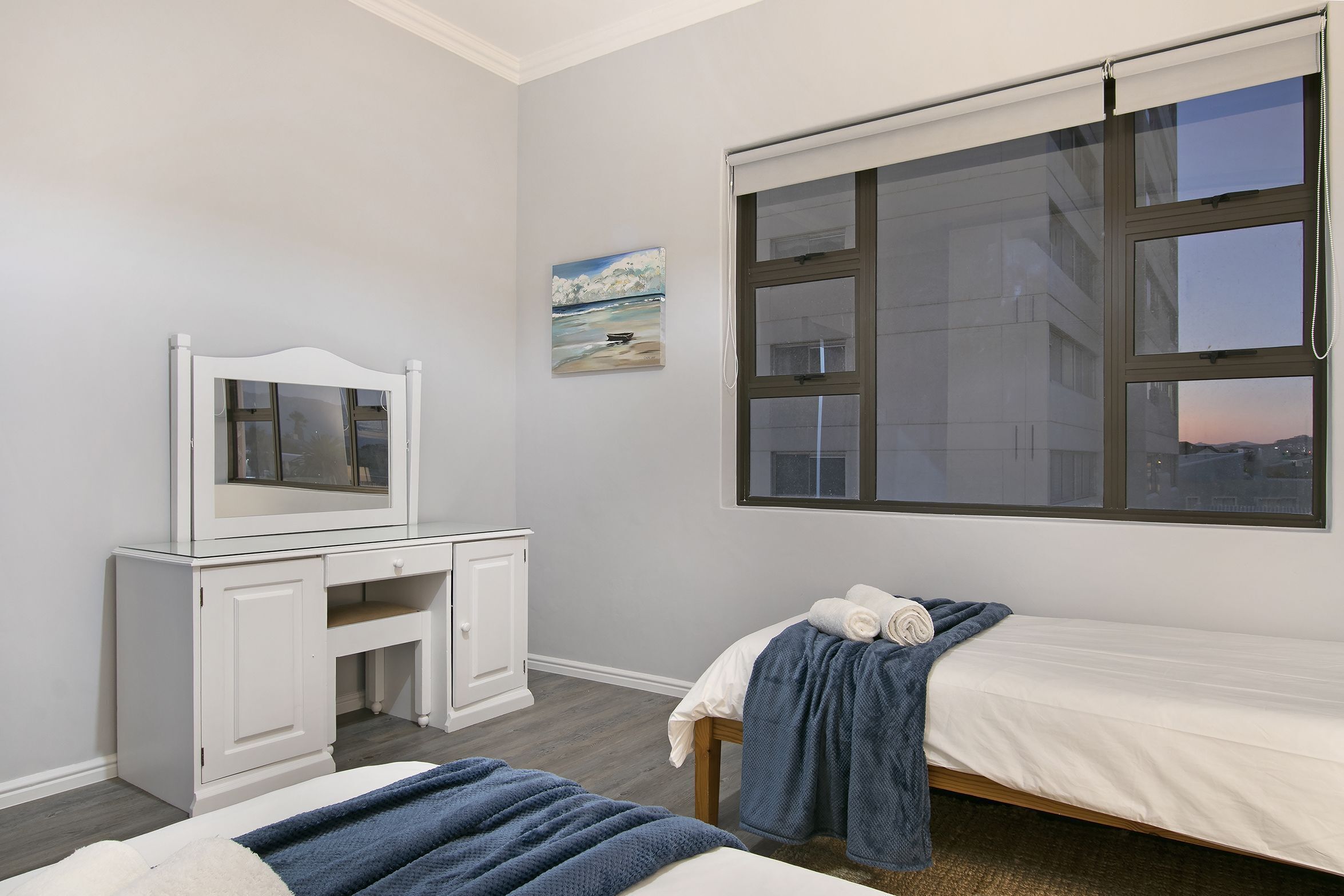 A bedroom with a bed, a desk, a chair, a window with blinds, and a painting on the wall.