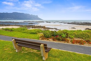 Un banc installé sur une pelouse, avec un sentier qui mène à une plage rocheuse et à l’océan.