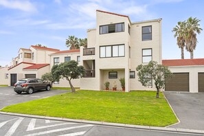 Un edificio residencial de varios pisos con techo plano, zona de estacionamiento y césped bien cuidado.