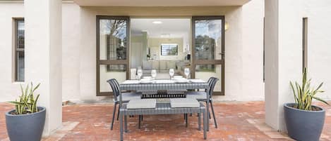 An outdoor dining area with a table set for four, surrounded by chairs with striped cushions.
