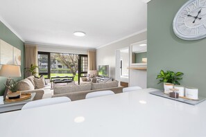 Un salon moderne avec un coin repas, de grandes fenêtres et une horloge au mur.
