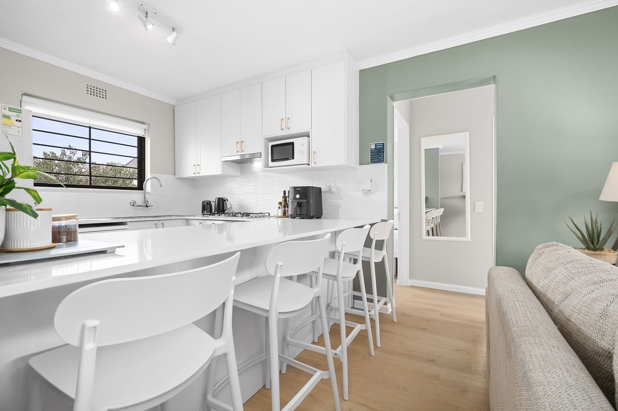 A modern kitchen with white cabinets, a central island with bar stools, a microwave, and a coffee maker.
