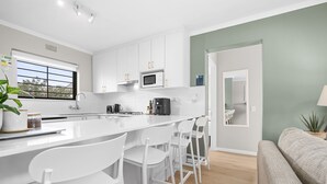 Una cocina moderna con armarios blancos, una isla central con taburetes y electrodomésticos como microondas y cafetera.